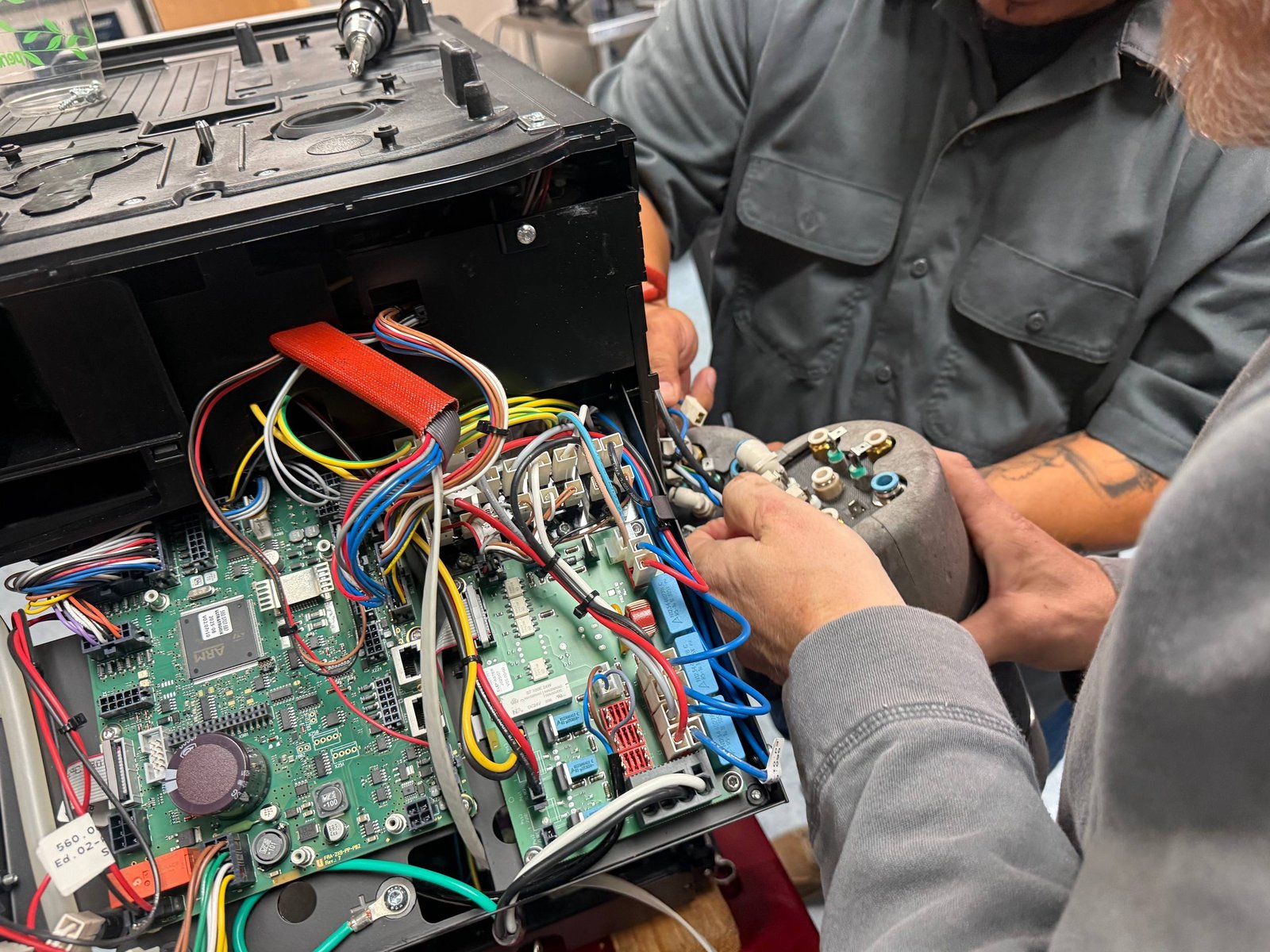 Instructor's hands inspecting wiring inside an open Franke coffee machine