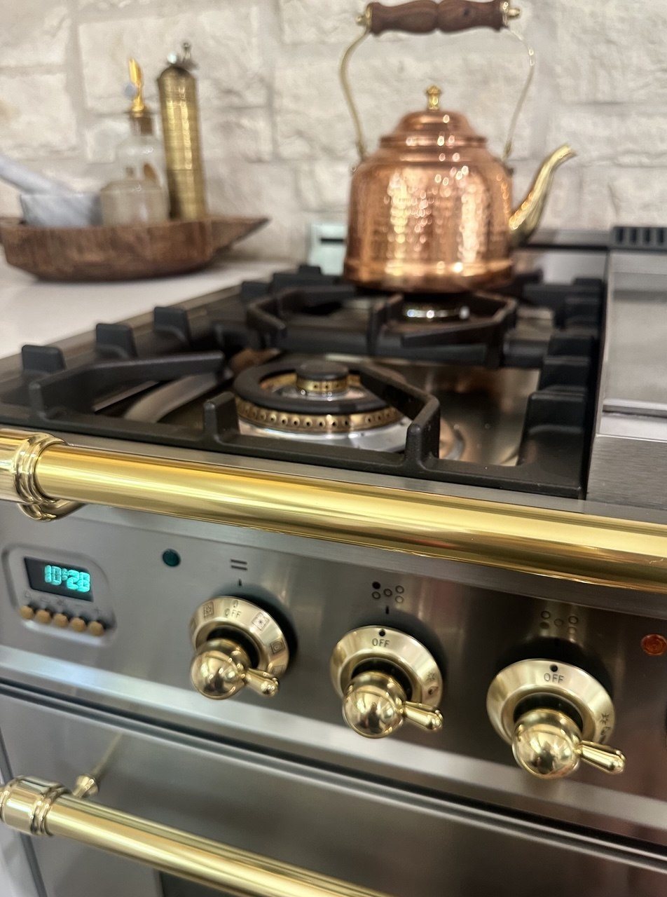 Copper kettle on an ILVE burner above brass control knobs