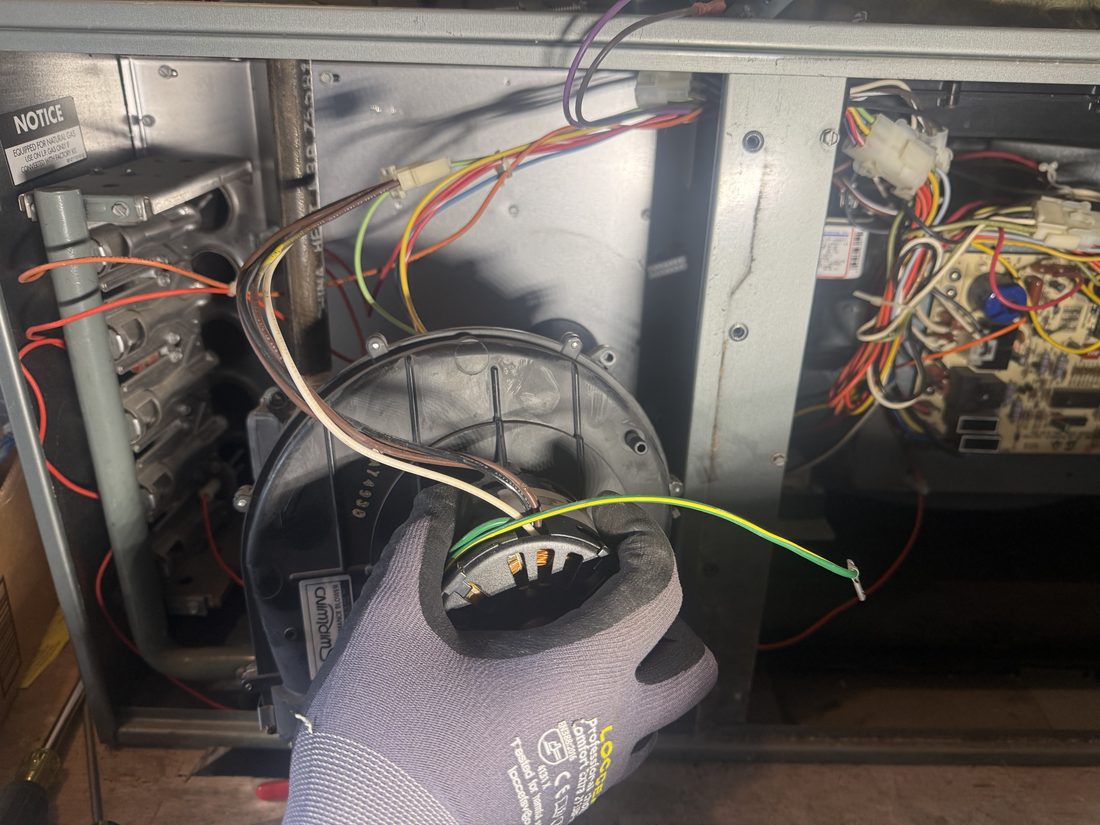 Technician fitting a new draft-inducer motor into an open Ruud gas furnace cabinet during a repair in Alamo