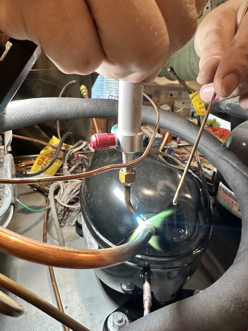 ADRIUM technician brazing a copper refrigerant line onto a compressor with a torch during a sealed-system repair